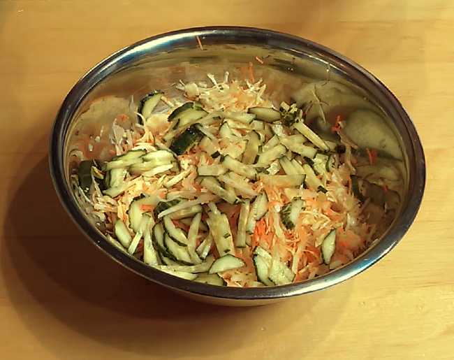 В миску выкладываем перетёртую капусту, лук, добавляем морковь - перемешиваем. Затем добавляем нашинкованный огурец - перемешиваем.
